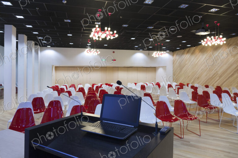 A laptop computer at a podium and rows of chairs in a large room