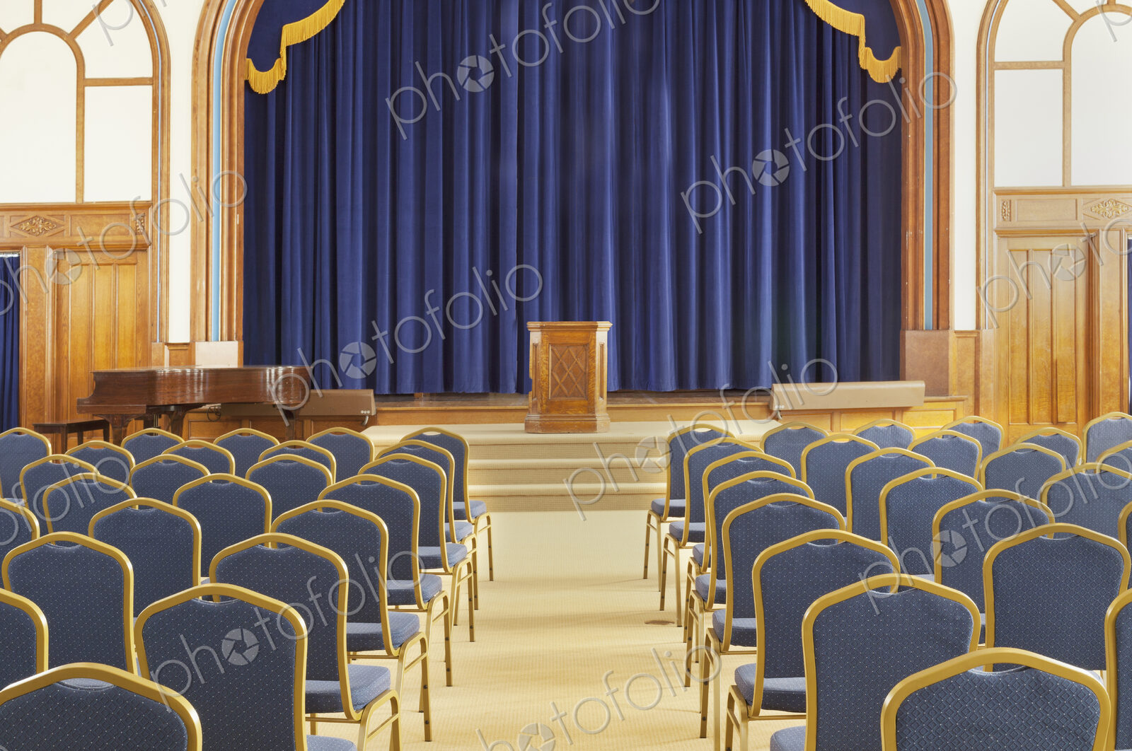 A large auditorium in a historic building, with blue chairs. View to the stage and podium.