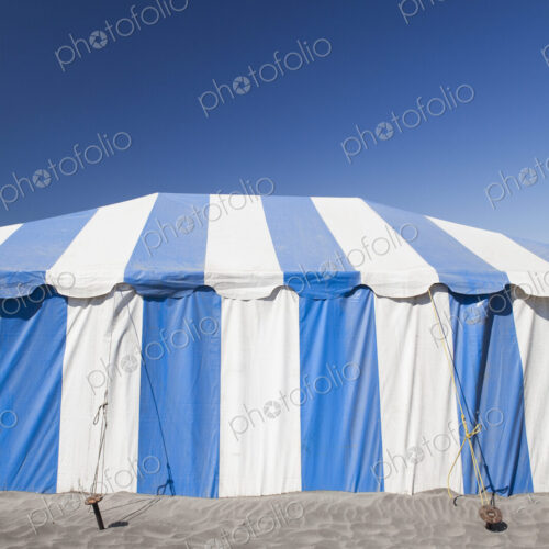 A large blue and white striped tent or marquee on a beach