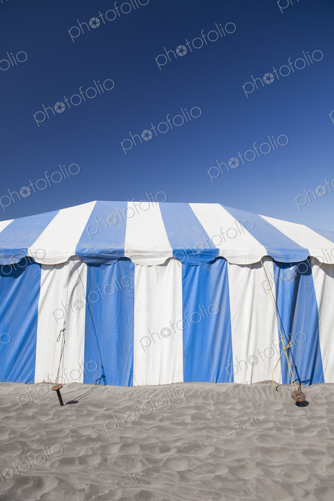 A large blue and white striped tent or marquee on a beach