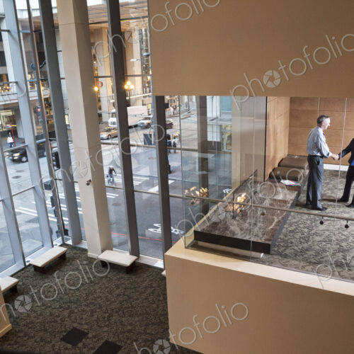 A large building, lobby, view looking into an office with glass walls, two business…