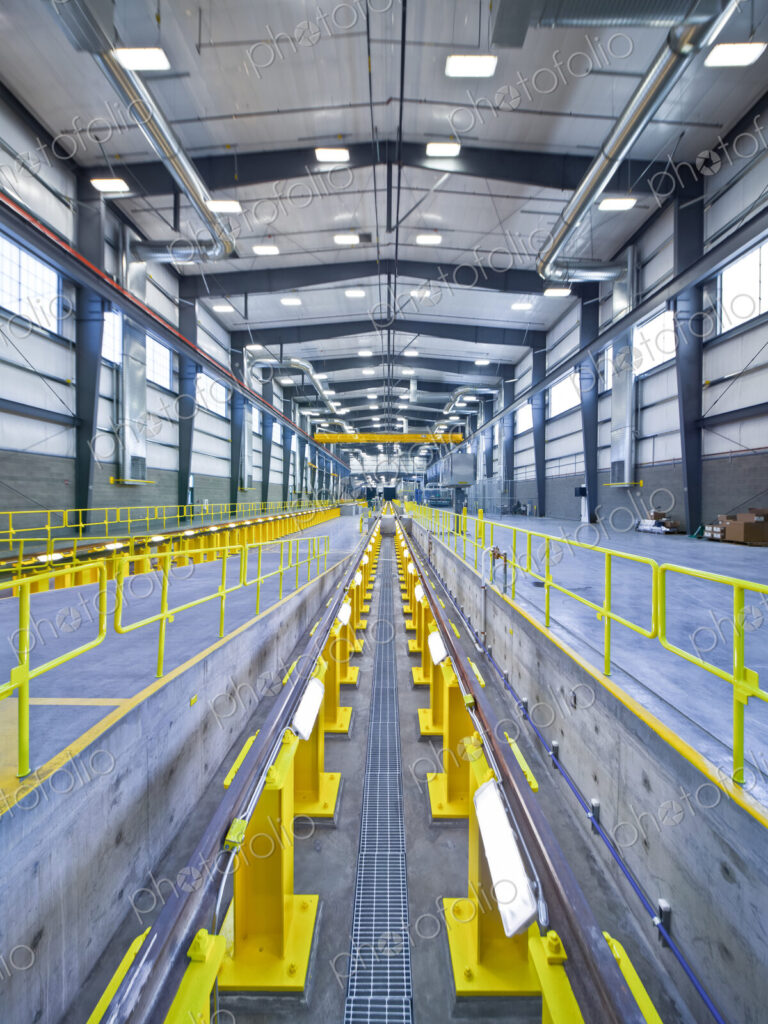 A large covered maintenance yard on a railway, an elevated rail avobe a pit for…