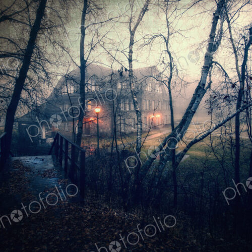 A large house at dusk with lights glowing. Woodland. A footbridge. A large house at dusk with lights glowing. Woodland. A footbridge.