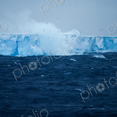 A large iceberg with steep sides, floating on the water. Waves and spray rising.… A large iceberg with steep sides, floating on the water. Waves and spray rising.…