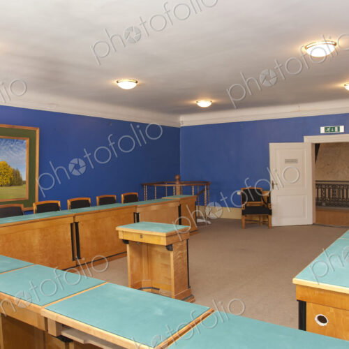 A large meeting room, with desks and chair and central podium, old fashioned decor,…
