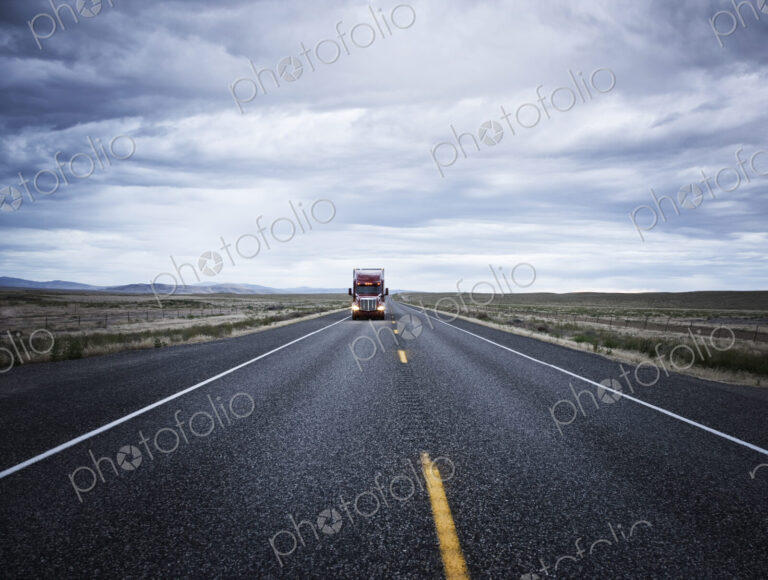 A large red commercial truck on the highway, in the distance