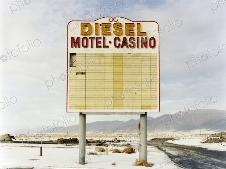 A large roadside sign in a flat landscape with light snow. Mountain range. Diesel and…