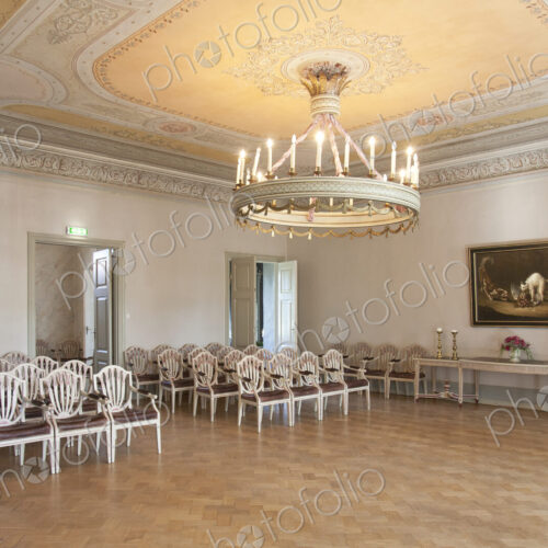 A large room with parquet flooring, elegant chairs and tables, chandelier and dance floor.