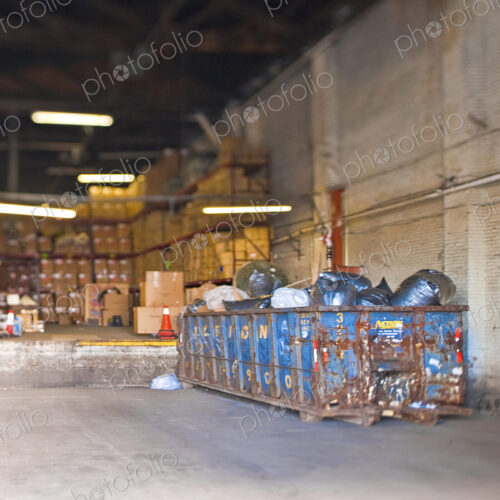 A large storage facility with loading bay, racks of boxes and large refuse skip