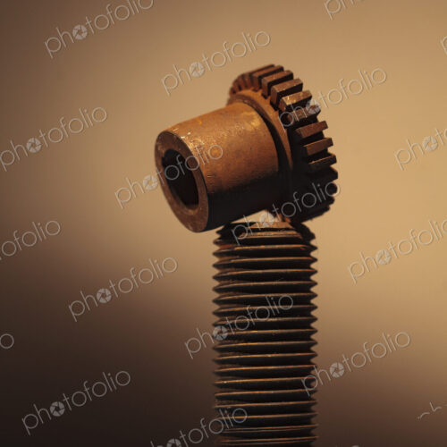 A large upright bolt with a thread and a bolt with cog notches. A large upright bolt with a thread and a bolt with cog notches.