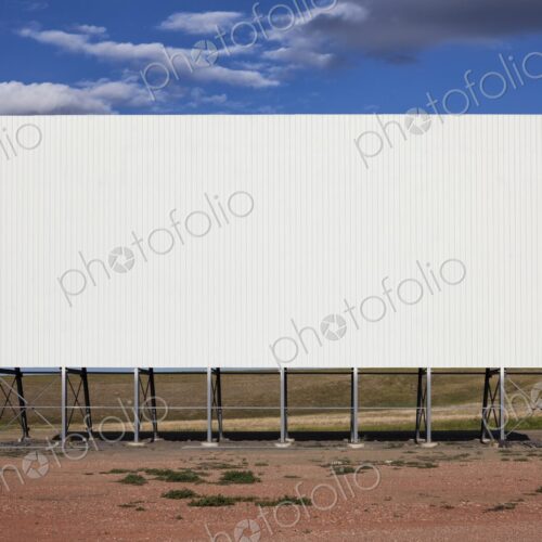 A large white drive in movie screen stands on the prairie beneath a wide blue sky with… A large white drive in movie screen stands on the prairie beneath a wide blue sky with…