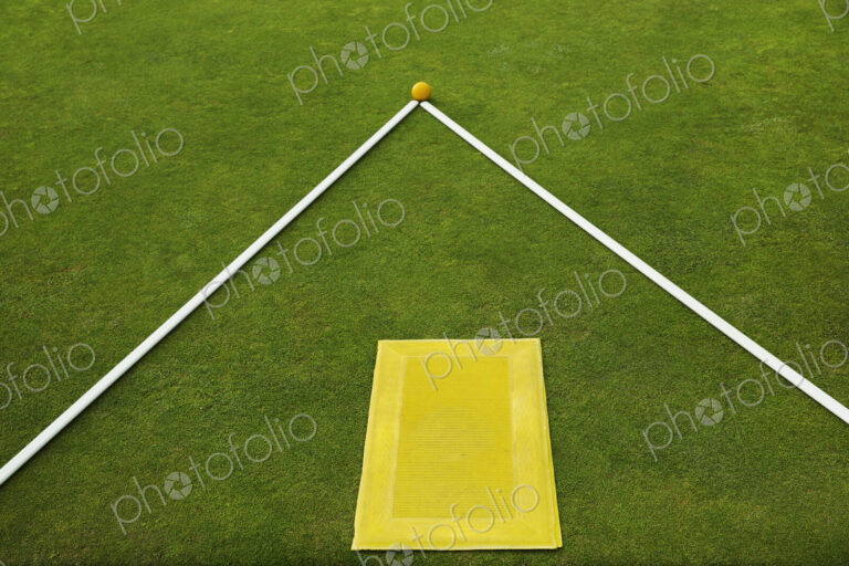 A lawn bowls green edge, a yellow player's mat to stand on and two white lengths of…