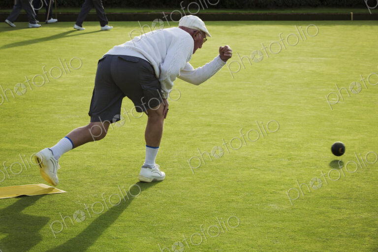 A lawn bowls player standing on a small yellow mat preparing to deliver a bowl down…