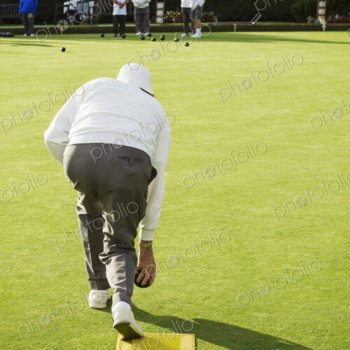 A lawn bowls player standing on a small yellow mat preparing to deliver a bowl down… A lawn bowls player standing on a small yellow mat preparing to deliver a bowl down…