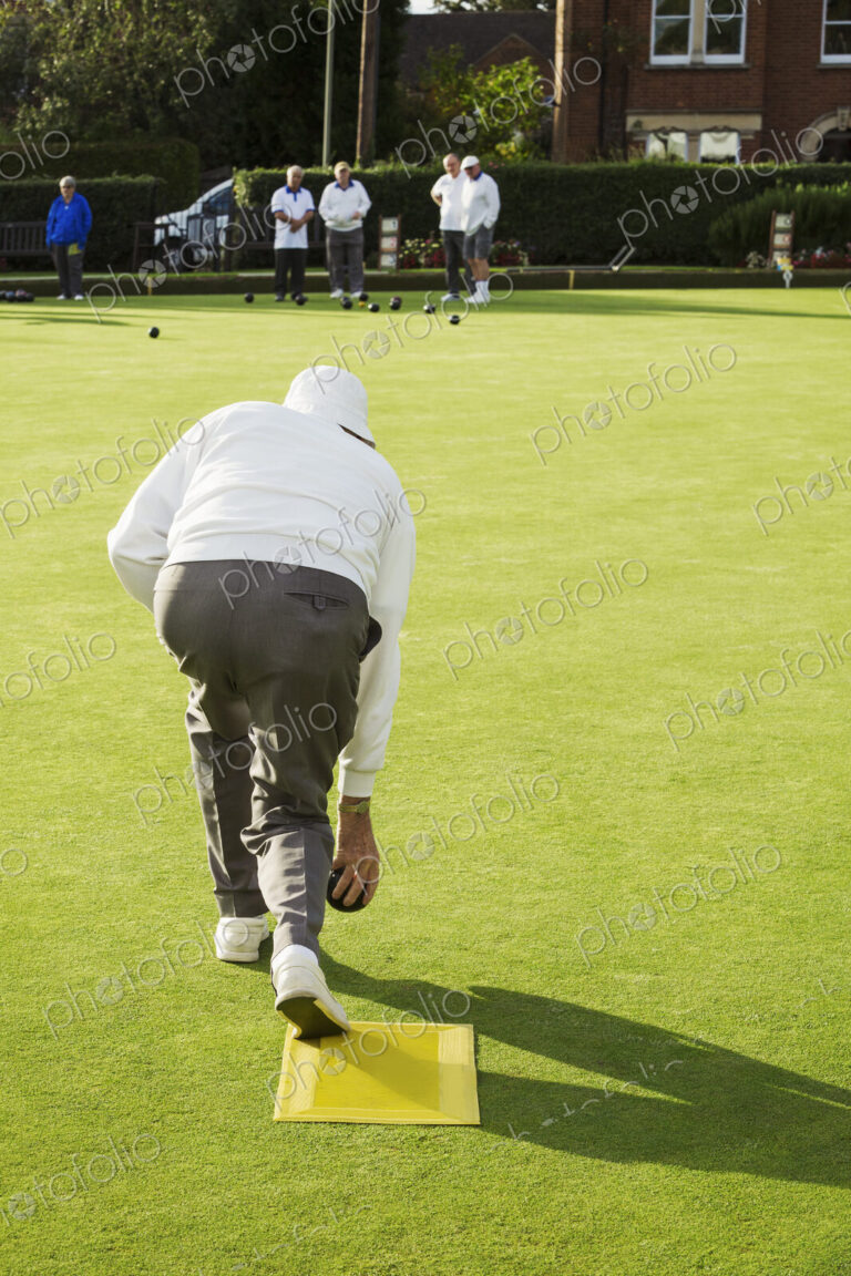 A lawn bowls player standing on a small yellow mat preparing to deliver a bowl down…