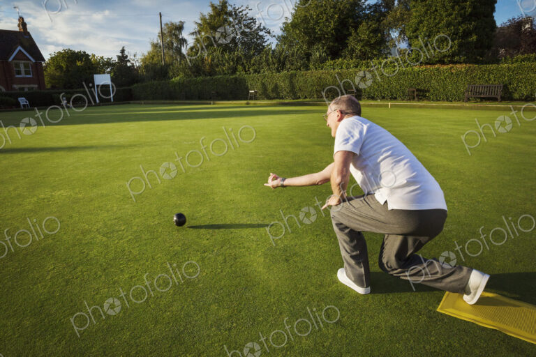 A lawn bowls player standing on a small yellow mat preparing to deliver a bowl down…
