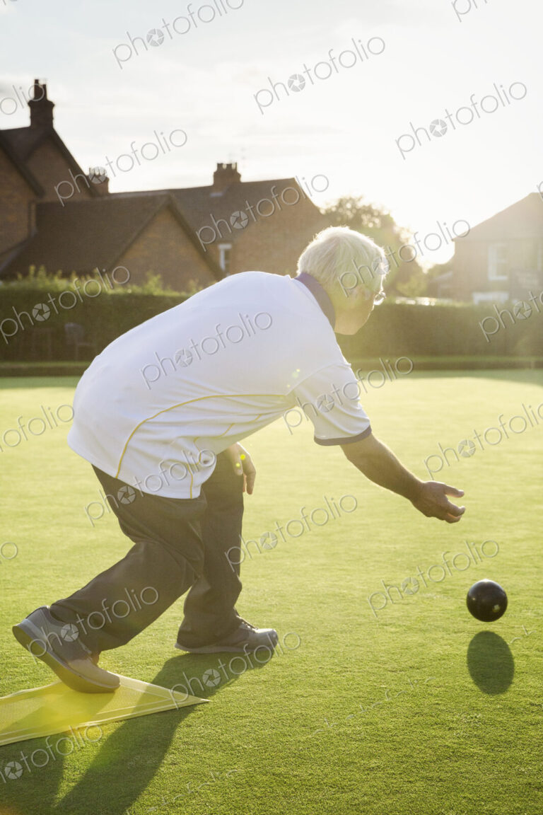 A lawn bowls player standing on a small yellow mat preparing to deliver a bowl down…