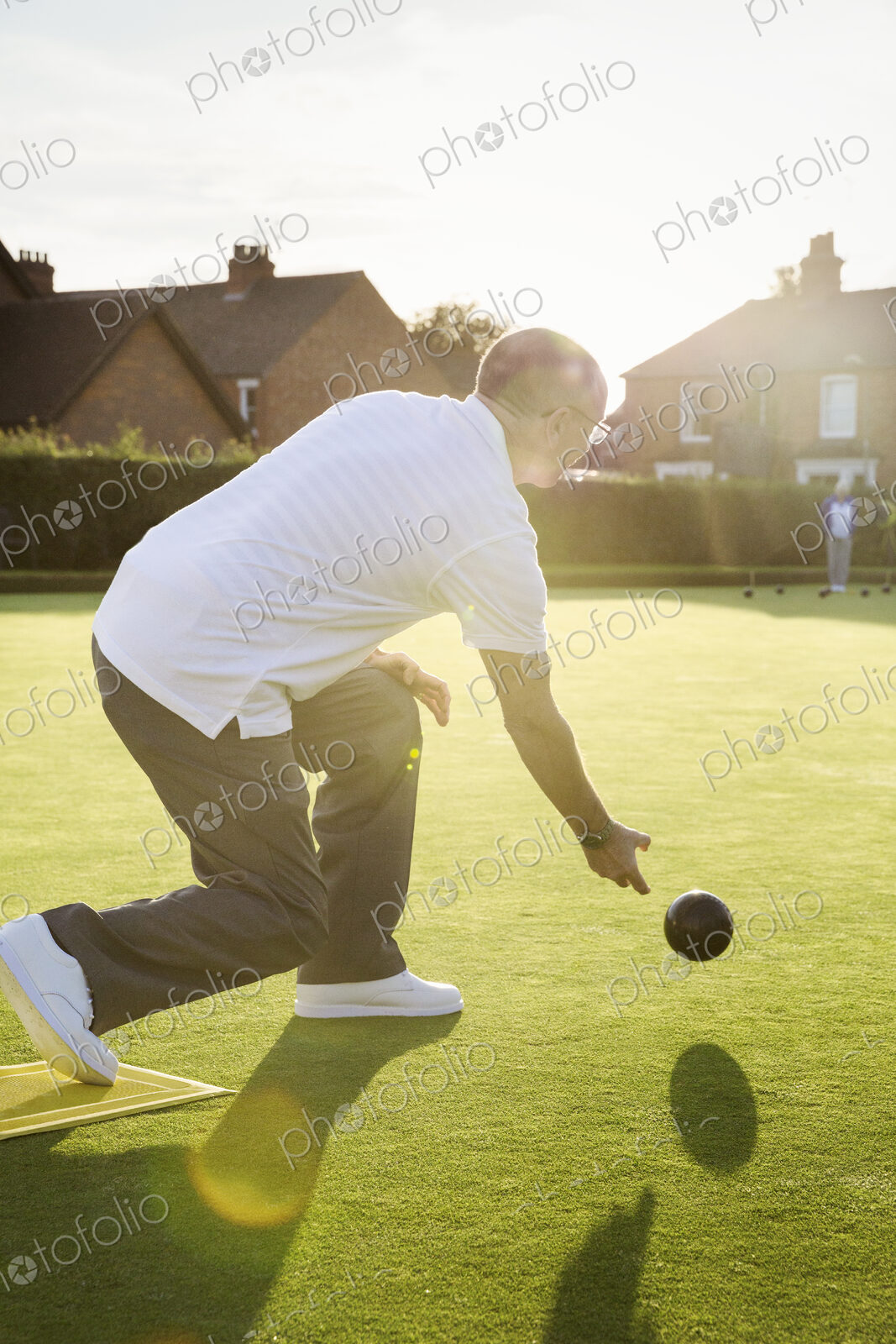 A lawn bowls player standing on a small yellow mat preparing to deliver a bowl down…