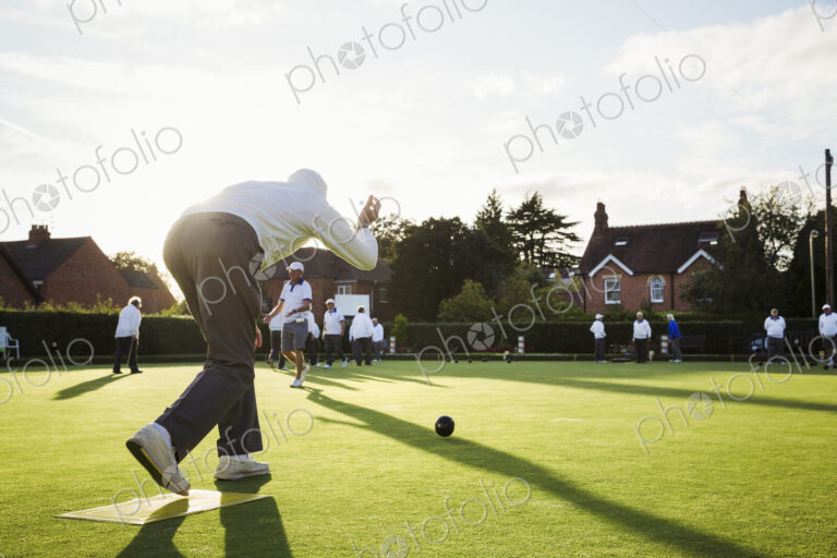 A lawn bowls player standing on a small yellow mat preparing to deliver a bowl down…