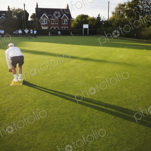 A lawn bowls player standing on a small yellow mat preparing to deliver a bowl down… A lawn bowls player standing on a small yellow mat preparing to deliver a bowl down…