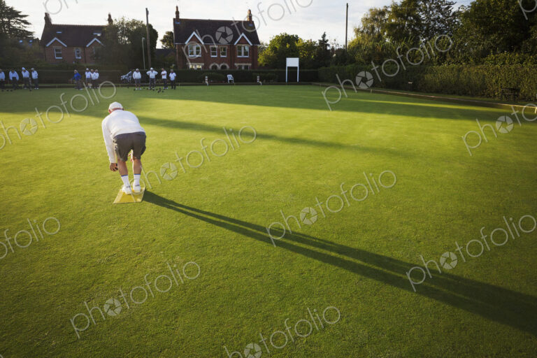 A lawn bowls player standing on a small yellow mat preparing to deliver a bowl down…