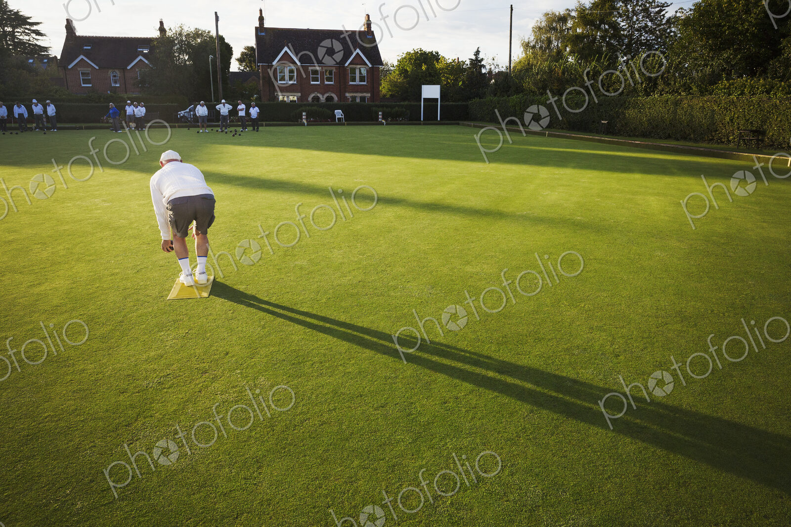 A lawn bowls player standing on a small yellow mat preparing to deliver a bowl down…
