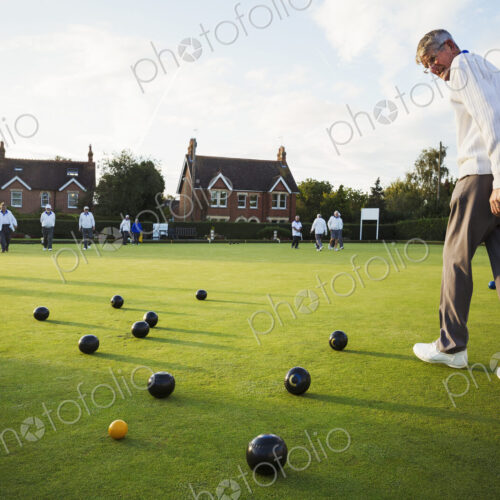 A lawn bowls player walking across the green, the playing surface, at an end with… A lawn bowls player walking across the green, the playing surface, at an end with…