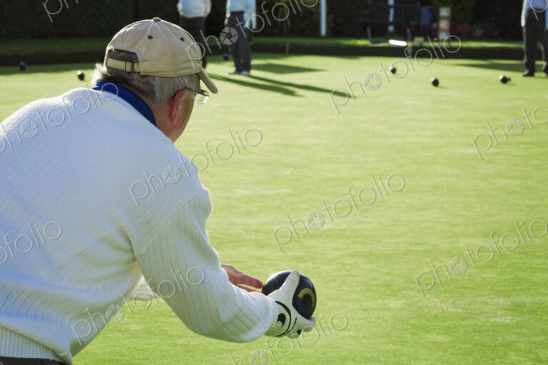 A lawn bowls player wearing a glove, holding and preparing to deliver a bowl down the…