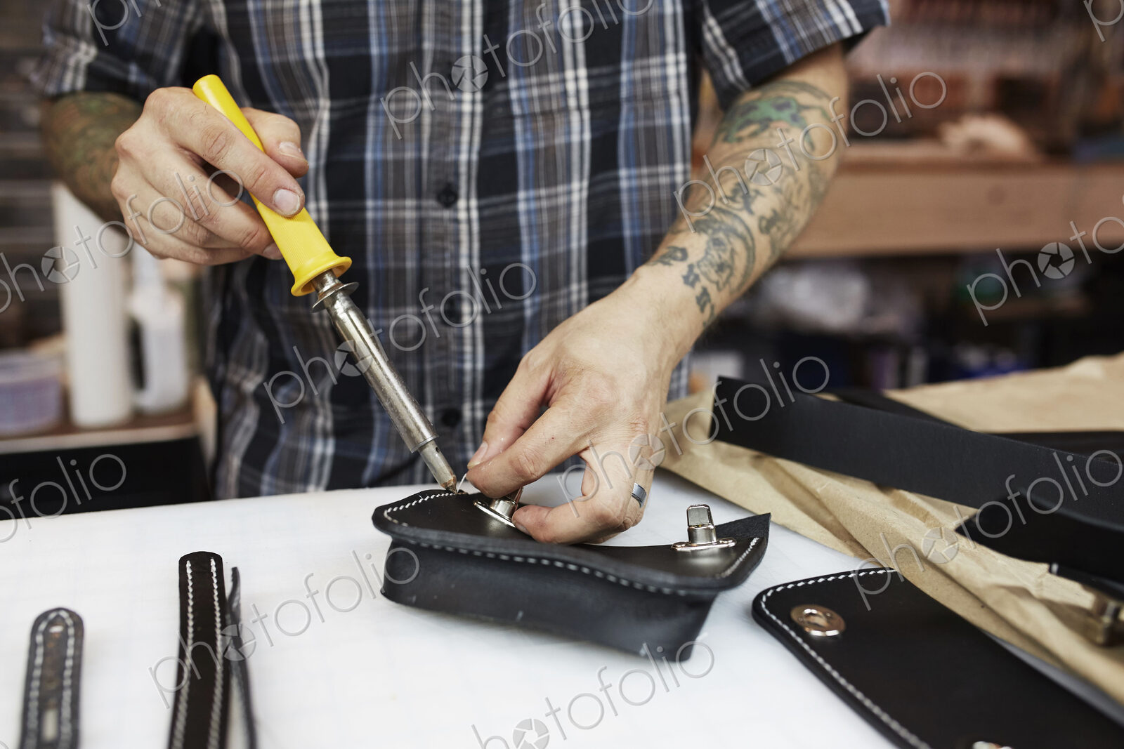 A leather worker and craftsman using a hand held tool on a blue leather bag on a workbench