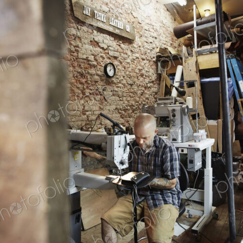 A leather worker, craftsman using an industrial sewing machine on leather material ion…