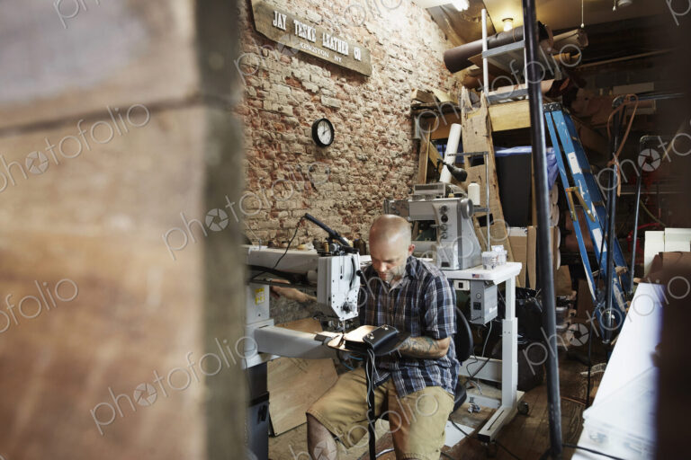 A leather worker, craftsman using an industrial sewing machine on leather material ion…