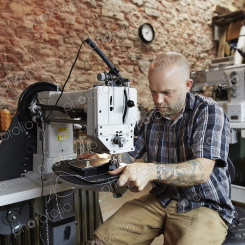 A leather worker, craftsman using an industrial sewing machine on leather material,… A leather worker, craftsman using an industrial sewing machine on leather material,…