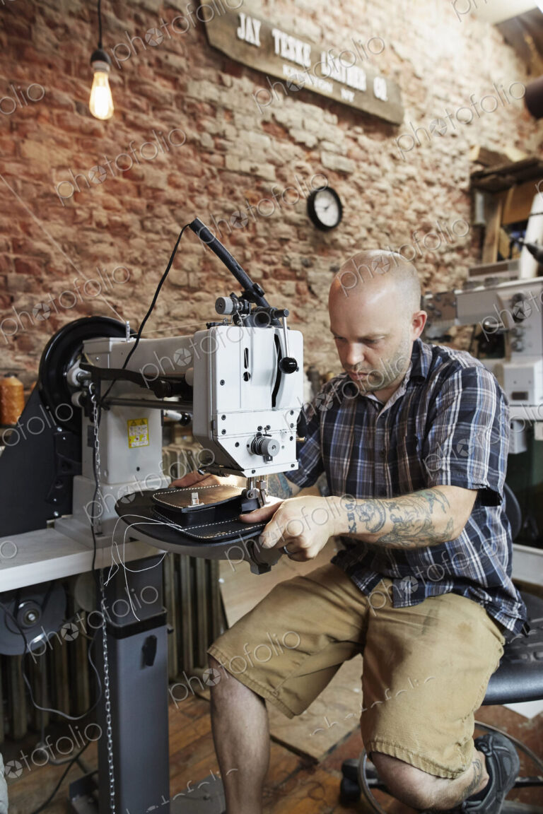 A leather worker, craftsman using an industrial sewing machine on leather material,…