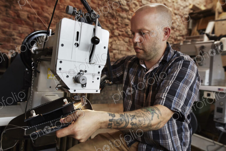 A leather worker, craftsman using an industrial sewing machine on leather material,…