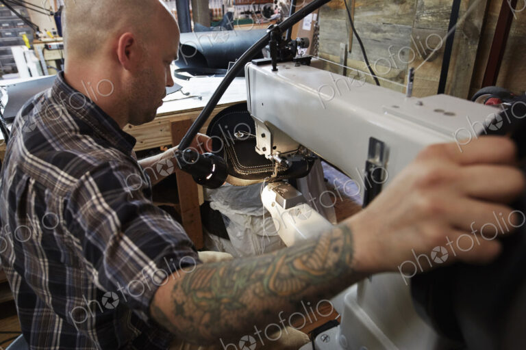 A leather worker, craftsman using an industrial sewing machine on leather material,…