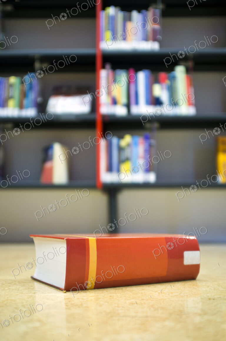 A library book on the floor in front of a bookshelf in a public library, space on the…