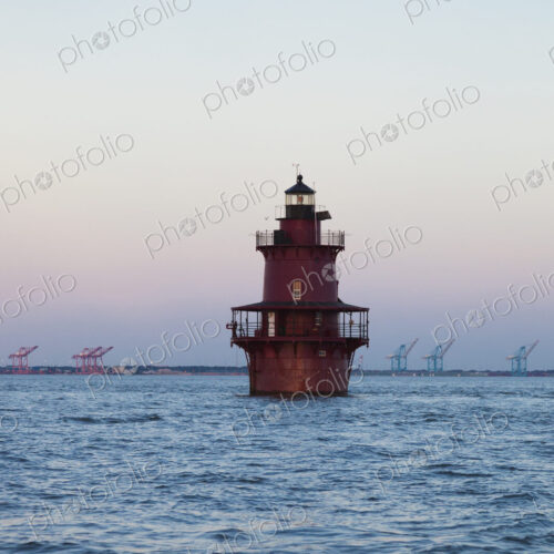 A lighthouse in Chesapeake Bay, view of the coastline with large lifting cranes of the… A lighthouse in Chesapeake Bay, view of the coastline with large lifting cranes of the…