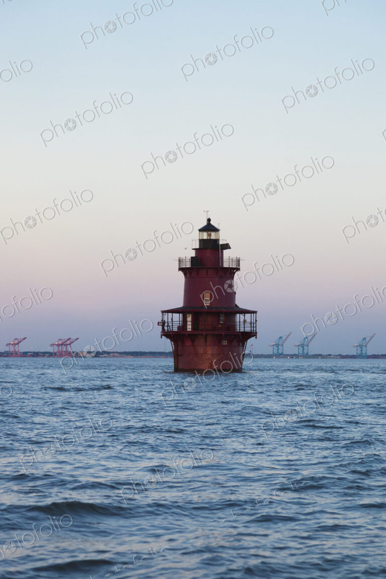 A lighthouse in Chesapeake Bay, view of the coastline with large lifting cranes of the…