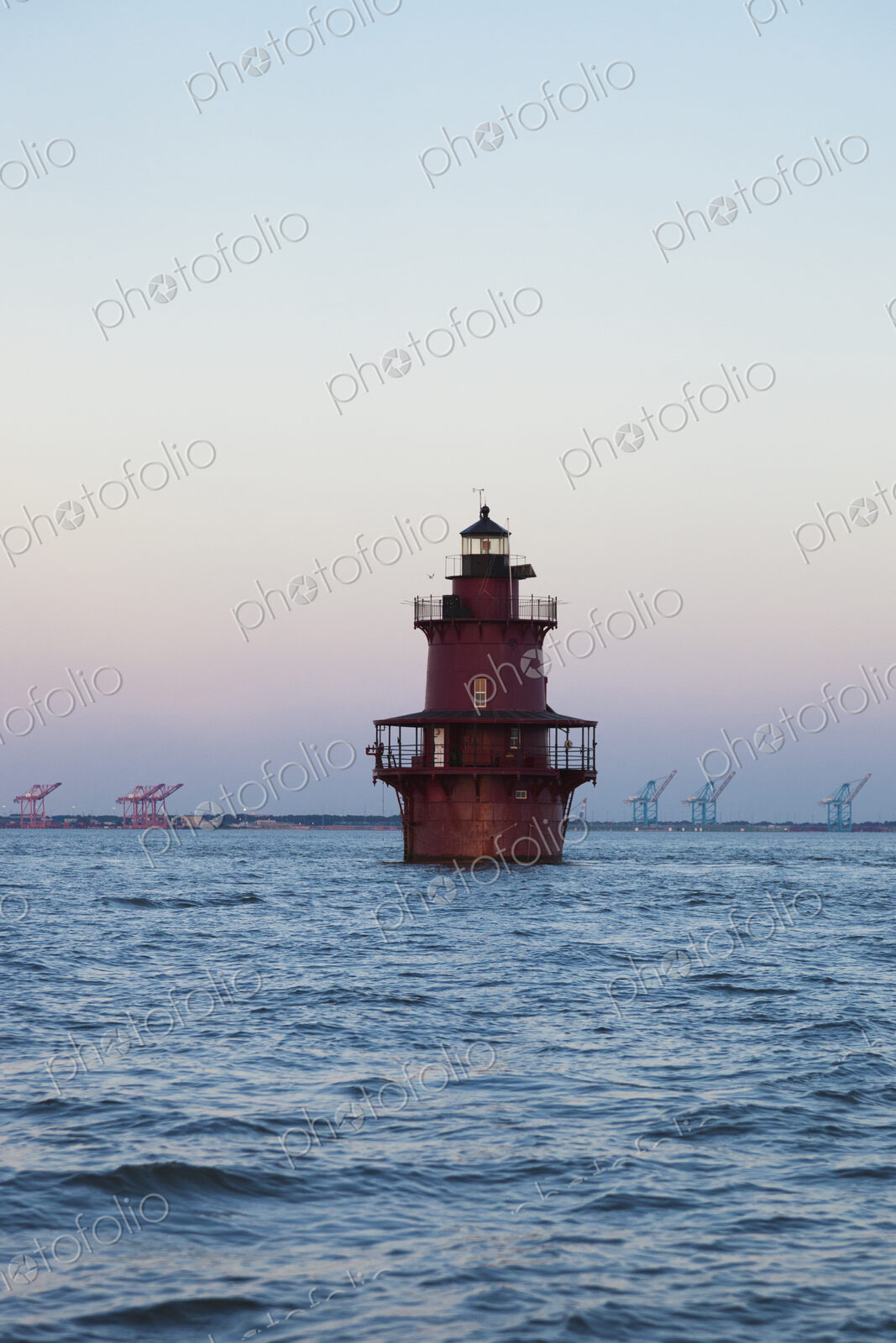 A lighthouse in Chesapeake Bay, view of the coastline with large lifting cranes of the…