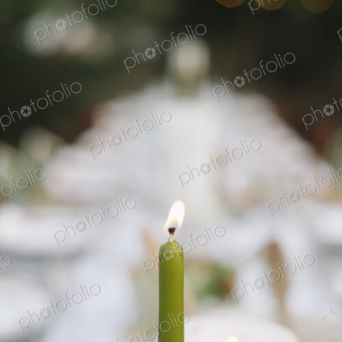 A lit candle on a table set with plates and glasses, food and drink in a garden. A lit candle on a table set with plates and glasses, food and drink in a garden.