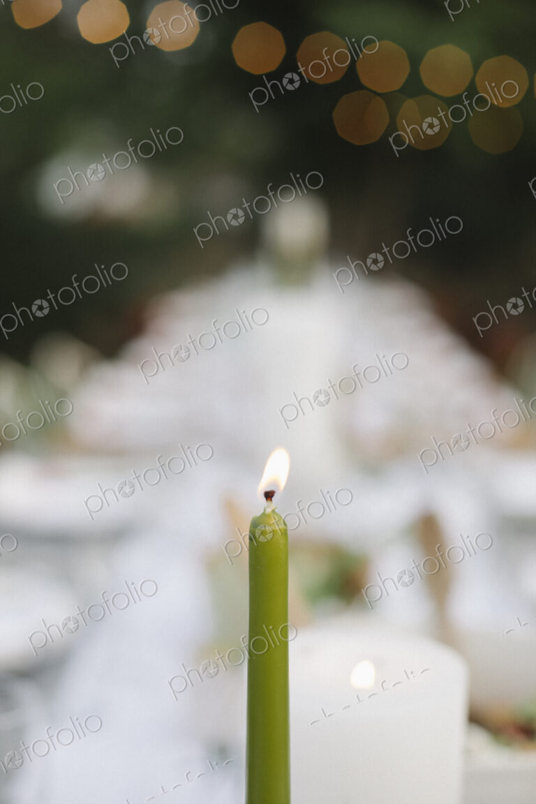 A lit candle on a table set with plates and glasses, food and drink in a garden.
