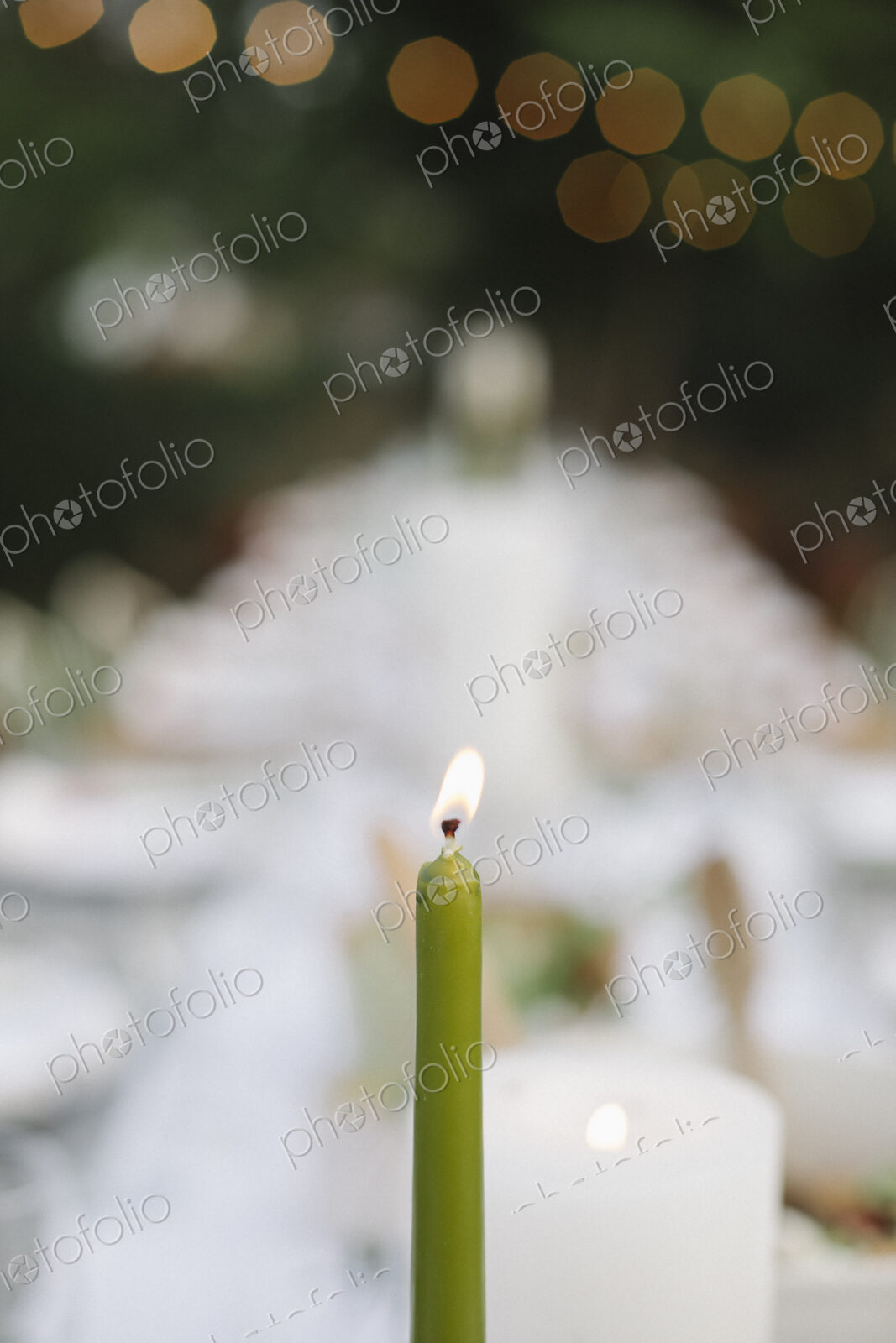 A lit candle on a table set with plates and glasses, food and drink in a garden.