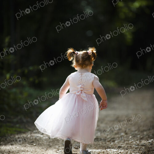 A little girl, a bridesmaid in a pink dress running along a path. A little girl, a bridesmaid in a pink dress running along a path.