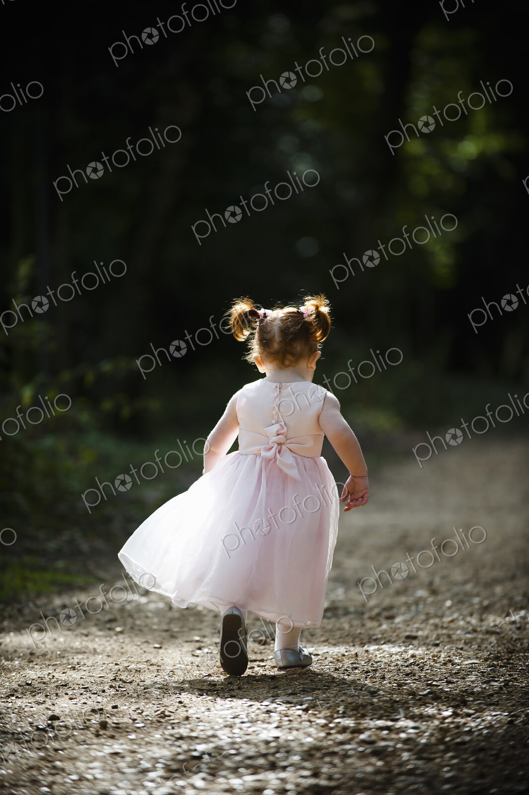 A little girl, a bridesmaid in a pink dress running along a path.