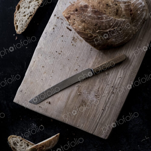 A loaf of brown bread on a board and a bread knife A loaf of brown bread on a board and a bread knife
