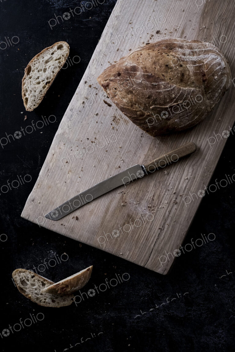 A loaf of brown bread on a board and a bread knife