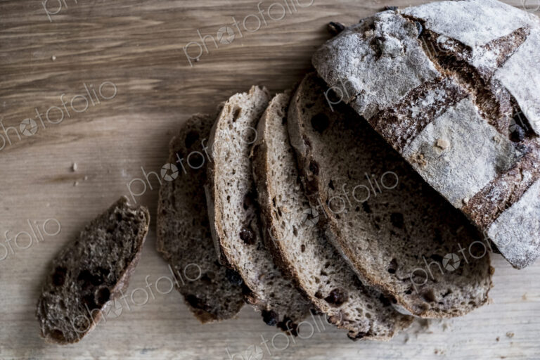 A loaf of fresh sliced brown bread on a bread board and a sharp knife