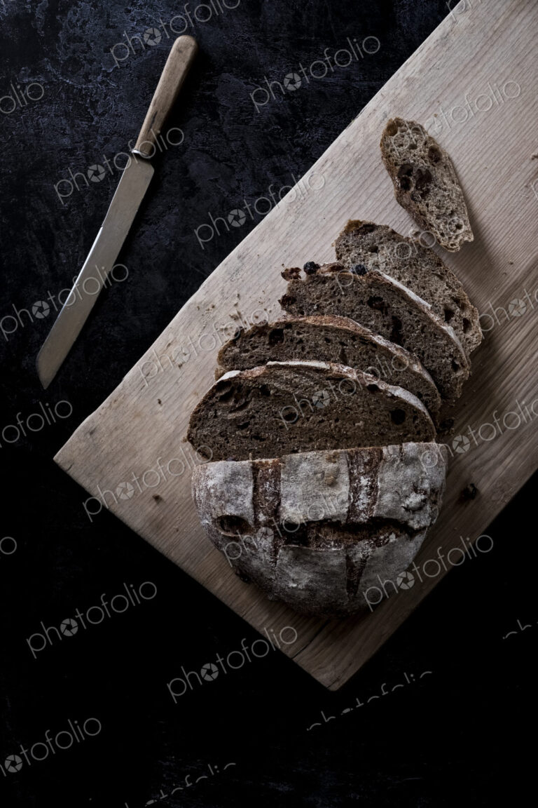 A loaf of fresh sliced brown bread on a bread board and a sharp knife