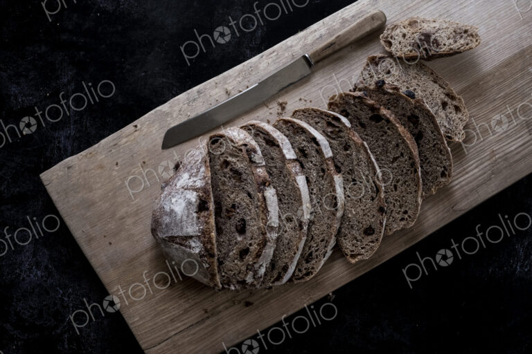 A loaf of fresh sliced brown bread on a bread board and a sharp knife
