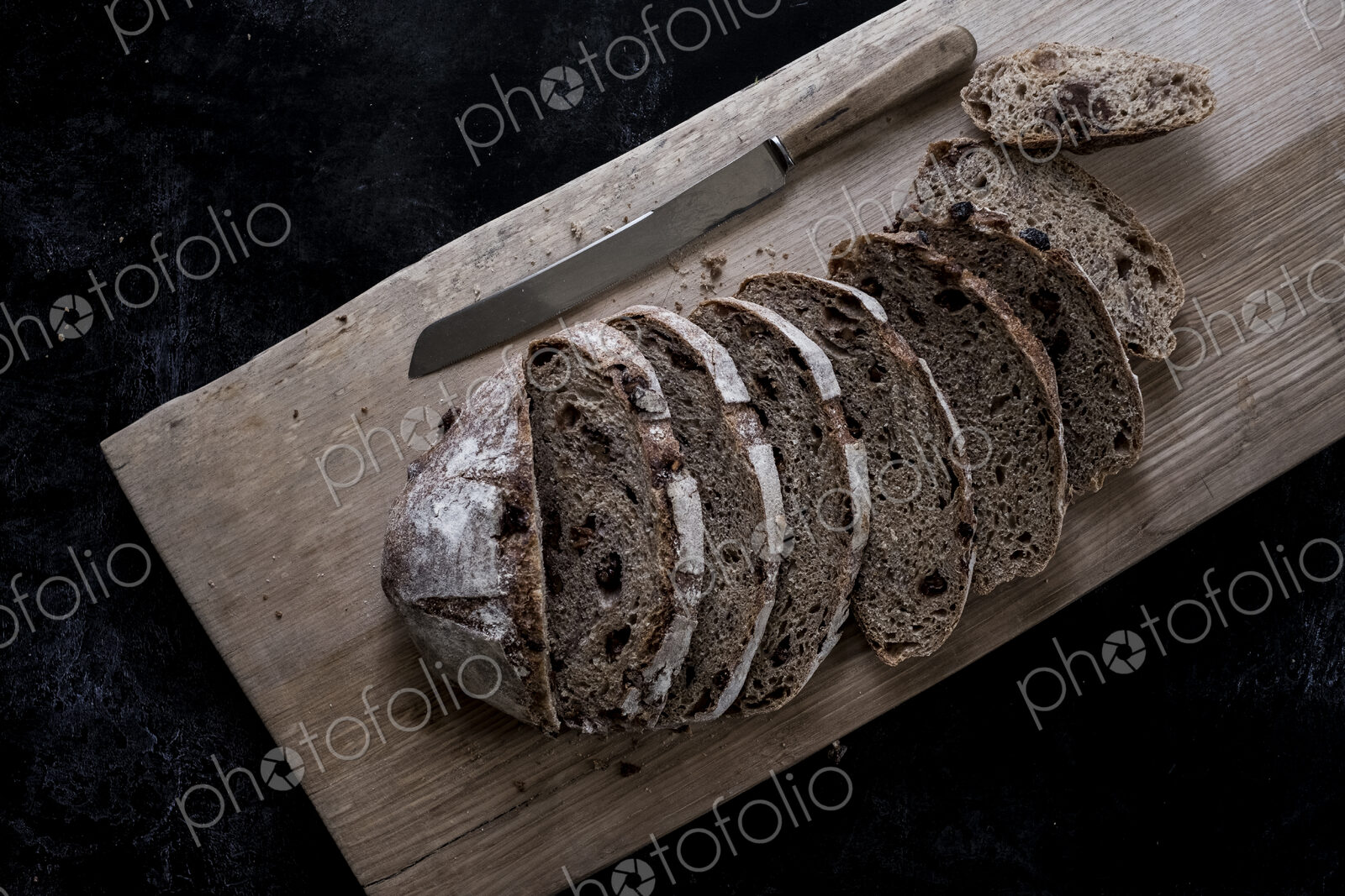 A loaf of fresh sliced brown bread on a bread board and a sharp knife